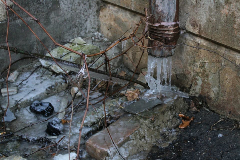 Icicles hanging from a rusted pipe at the foot of a wall