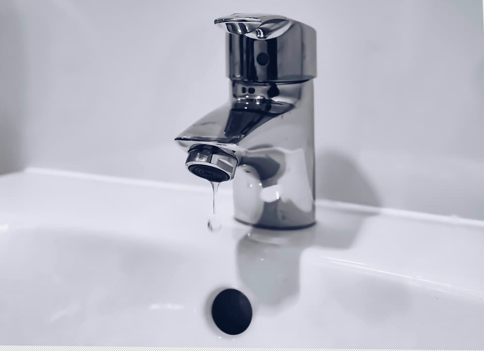 A chrome bathroom faucet dripping into a white sink